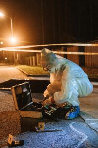 Forensic expert in protective gear examining evidence at a crime scene at night.