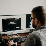 Man working on web design at home office setup with dual monitors.