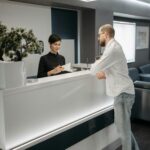 A man and woman at a sleek office reception desk, discussing paperwork in a professional setting.
