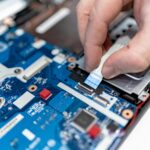 Close-up image of hands repairing a laptop circuit board showing intricate details of electronics.
